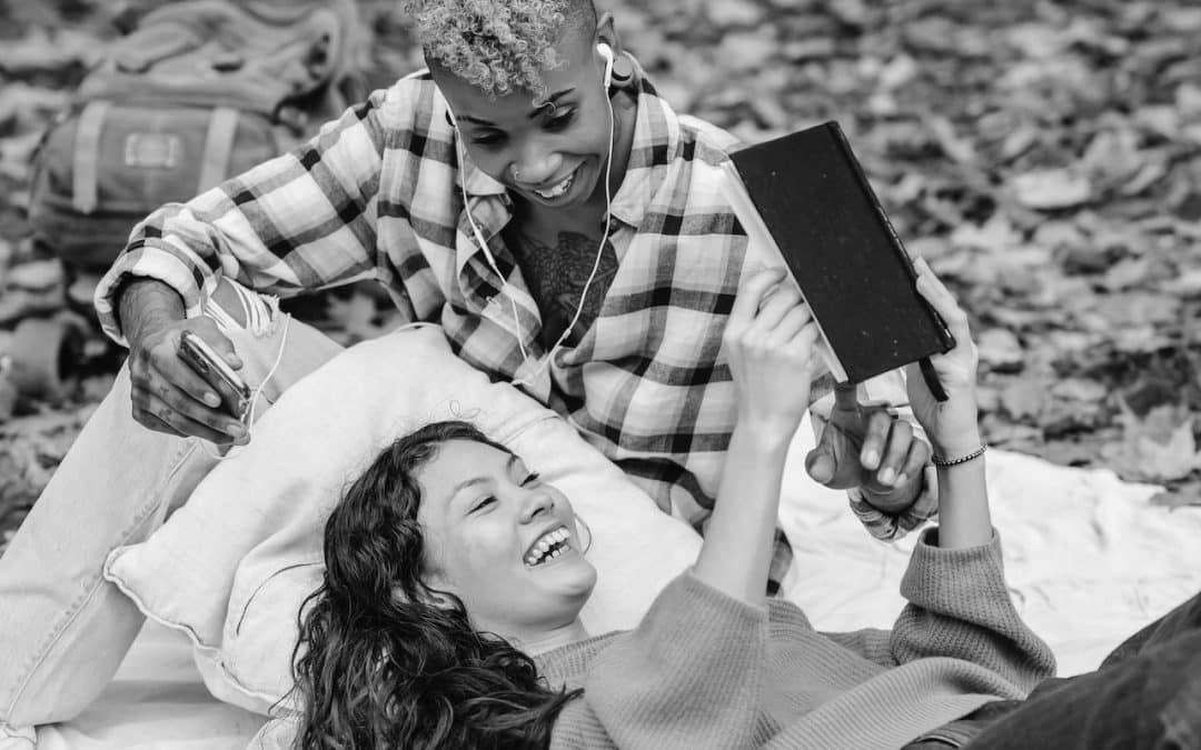 Two women reading a book and wearing earbuds