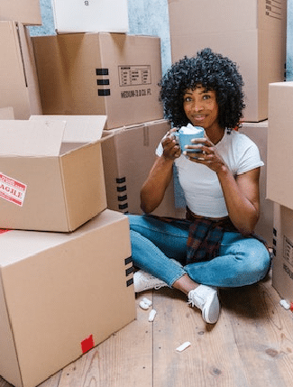 Black woman with natural hair sitting cross-legged between stacks of blank cardboard boxes